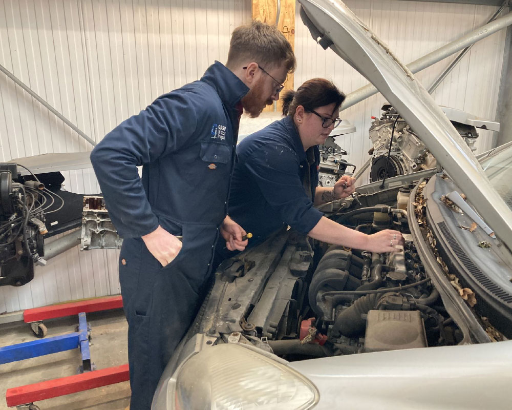 Young adult looking at car engine with mechanic